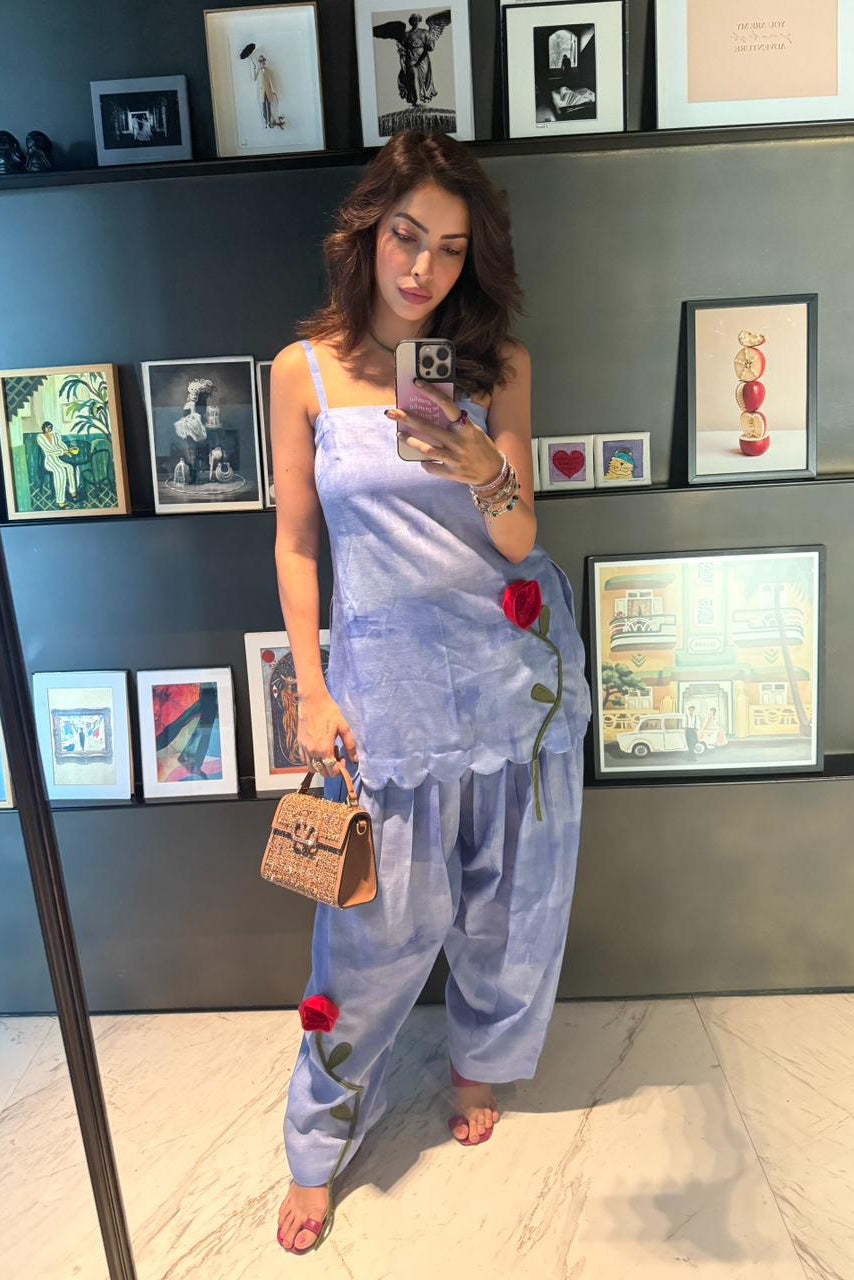 Woman in a light blue outfit with floral details standing in front of a wall with framed pictures.